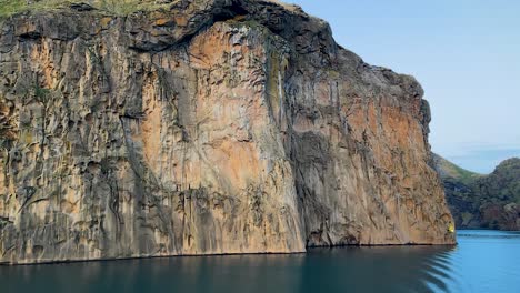 Majestätische-Felswand-Der-Vestmannaeyjar-Unter-Sanftem-Licht,-Blaues-Wasser-Im-Vordergrund
