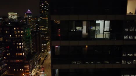 Night-view-of-lit-office-windows-in-a-Montreal-skyscraper,-city-lights-in-the-background,-urban-work-late-concept