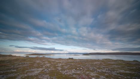 Thin-clouds-are-being-carried-by-strong-winds-over-the-rocky-coast-of-a-fjord-with-sparse-vegetation-in-a-timelapse-video