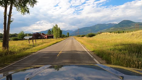 Small-village-and-mountain-range-in-horizon,-driving-POV-on-USA-country-road