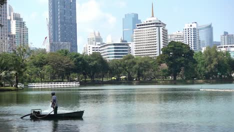 A-guy-in-a-boat-in-the-Lumphini-Park-in-Thailand-Bangkok,-with-the-skyline-in-the-background