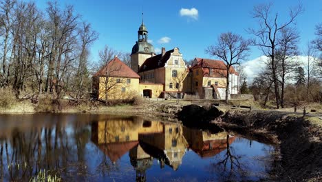 aerial-view-of-Lielstraupe-Castle-is-a-castle-Straupe-Parish,-Latvia-with-scenic-reflection-on-lake-still-water