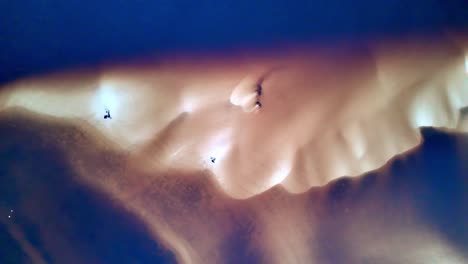 Aerial-view-of-sand-dunes-and-dark-water,-camera-pans-left,-dark-water-and-light-sand-dunes-create-texture,-birds-in-flight-visible