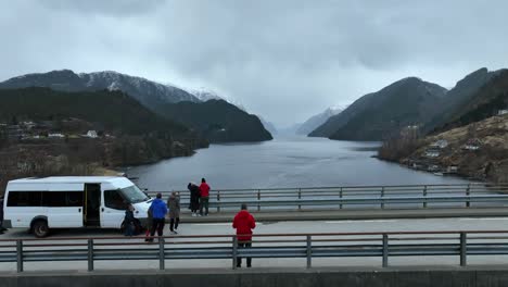 Tourists-exit-minibus-to-look-at-Norway-fjord-from-a-bridge-viewpoint,-aerial