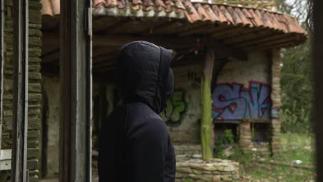 Young-man-with-mask-standing-outside-big-window-of-abandoned-mansion