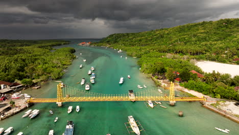 Puente-Amarillo-Sobre-Aguas-Cristalinas-Del-Mar-Con-Barcos-Pesqueros-Y-Veleros-En-Un-Día-Nublado-En-Nusa-Lembongan,-Indonesia