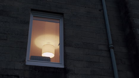 Window-with-lamp-on-inside,-filmed-from-street-at-night