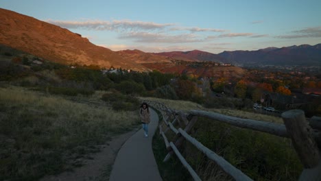 Woman-walks-up-paved-trail-near-Salt-Lake-City,-Utah-at-sunset-with-scenic-mountains