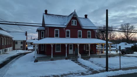 Toma-Aérea-De-Una-Casa-Unifamiliar-Nevada-Decorada-Con-Luces-Navideñas-En-La-Nieve-Del-Invierno