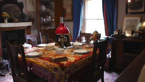 Antique-dining-room-set-with-ornate-tablecloth-and-china,-featuring-a-classic-oil-lamp