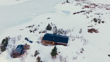 Aerial-View-Of-Mountain-Cabin-Surrounded-By-Thick-Snow-At-Winter