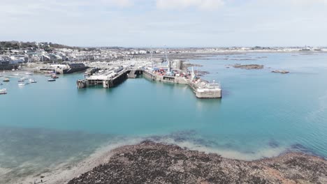Flight-over-St-Peter-Port-roof-tops-out-to-sea-over-harbour,Albert-Marina,fishing-fleet-model-yacht-pond-and-Castle-Cornet-with-views-of-islands-on-sunny-day