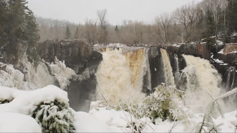 Waterfall-roars-with-power-in-a-snowstorm,-snow-swirls-around-the-cascading-water