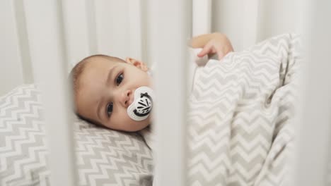 portrait-of-a-baby-girl-falling-asleep-in-a-crib-with-a-pacifier-in-her-mouth