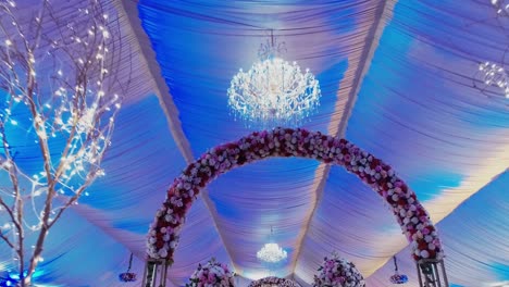 In-this-amazing-wedding-venue,-the-ceiling-features-a-lovely-chandelier-and-flower-decorations