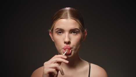 Naughty-caucasian-woman-licks-tasty-lollipop,-isolated-black-background