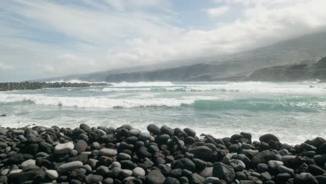 Slowmotion-group-of-surfers-surfing-on-ocean-waves,-pebble-beach,-Playa-Martiánez,-Puerto-de-la-Cruz,-Canary-Islands-in-spring