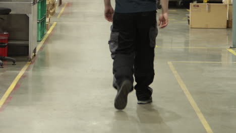 Logistic-warehouse-worker-walking-in-between-yellow-lines,-back-view