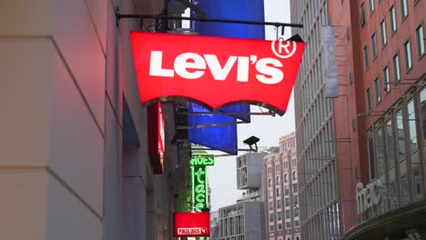 The-American-clothing-company-brand,-Levi's-store-and-logo-sign-on-a-commercial-retail-street-at-night