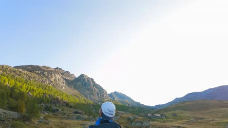 Tilt-Down-From-Clear-Blue-Sky-To-Reveal-Male-Hiker-Walking-Across-Wild-Meadow-Valley-In-Valmalenco-alps