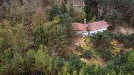 Vista-Aérea-Sobre-Una-Casa-Abandonada-En-Medio-Del-Bosque-Junto-A-Un-Lago