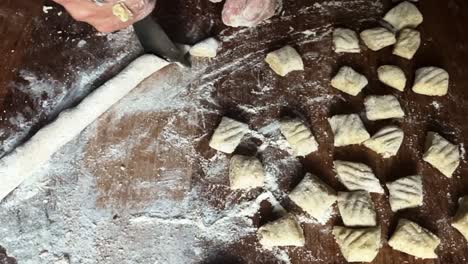 Kitchen-table-filled-with-gnocchi-pasta-preparation-chef-hands-closeup-italian-cuisine,-traditional-pasta,-slow-motion-knife-cutting-flour-dough