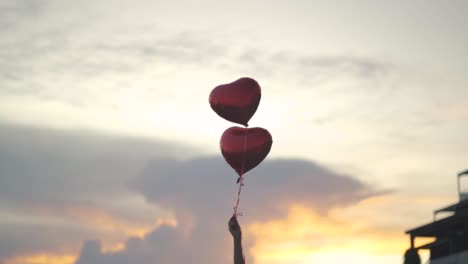 Zwei-Herzförmige-Luftballons-Schweben-In-Der-Luft,-Gehalten-Von-Einer-Frau