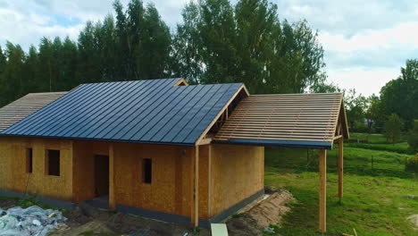 Holzhaus-Mit-Sonnenkollektoren-Im-Bau,-Lage-In-Grüner-Landschaft,-Luftaufnahme-Der-Spitze-Der-Wohnindustrie-Im-Gange