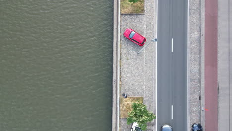 Overhead-Downward-Aerial-of-Canal-Alongside-Road-with-Red-Car-Parked,-in-Ghent