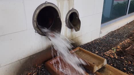 This-is-a-short-video-of-a-large-amount-of-water,-flowing-out-of-a-drainage-pipe,-on-the-side-of-a-building,-during-an-afternoon-thunderstorm