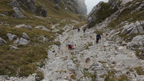 Cuatro-Excursionistas-Caminando-En-La-Montaña-Rocosa-De-Resegone-En-El-Norte-De-Italia-Con-Nubes-En-El-Fondo