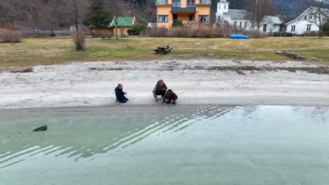 Mutter-Und-Kinder-Spielen-Im-Kalten-Wasser-Am-Strand,-Vater-Kommt-Ins-Bild,-Um-Ein-Foto-Zu-Machen