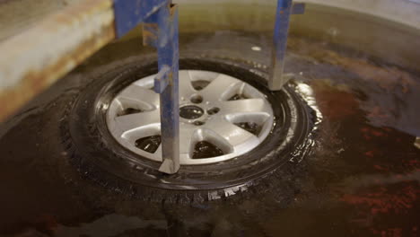 Plunging-leaky-tyre-into-water-to-check-for-bubbles-at-workshop,-close-up