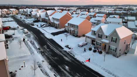 Menschen,-Die-Schnee-Räumen,-Und-Kinder,-Die-Bei-Sonnenuntergang-Im-Winter-In-Einem-Amerikanischen-Viertel-Auf-Schlitten-Spielen