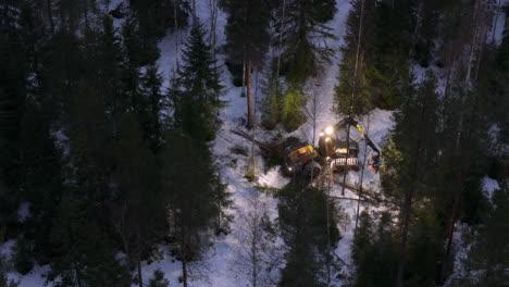 Harvester-felling-delimbing-and-bucking-trees-at-dawn-in-snowy-forest,-aerial