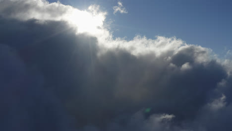 Drohnen-Schwenkansicht-Des-Hellen-Sonnenlichts,-Das-Durch-Weiße-Wolken-Unter-Einem-Blauen-Himmel-Scheint