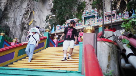 Gente-Caminando-Por-Escaleras-Pintadas-Con-Arcoíris-A-Través-De-Un-Acantilado-De-Piedra-Caliza-En-La-Entrada-De-Las-Cuevas-De-Batu-En-Selangor,-Malasia