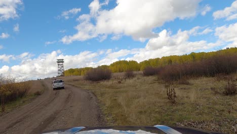 White-SUV-driving-by-on-gravel-road-near-lookout-tower,-front-POV-shot