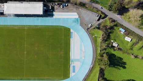 Aufsteigende-Aufnahme-Eines-Nicht-Genutzten-Sportstadions,-Das-An-Einem-Sonnigen-Tag-Spielfeld,-Laufbahn-Und-Tribüne-Zeigt