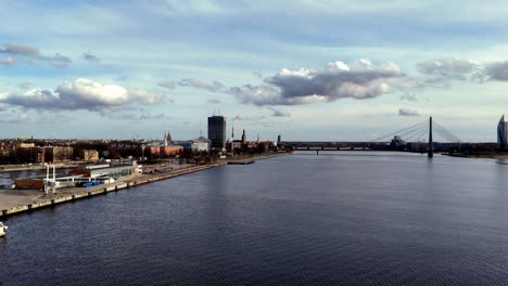 Riga-aerial-drone-cityscape-with-skyline-of-the-city-at-distance-during-a-clear-sunny-day-and-port-dock-over-the-sea