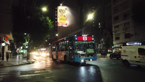Transit-at-rivadavia-avenue-night-car-traffic-autobus-commercial-area-capital-town-of-buenos-Aires-argentina,-nighttime-with-small-rain-weather