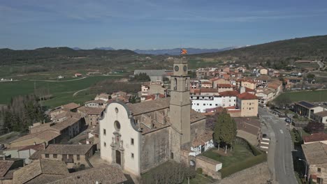 Vista-Aérea-Orbital-De-Un-Pequeño-Pueblo-Catalán-Con-Una-Torre-De-Reloj-Con-Una-Bandera-Independentista