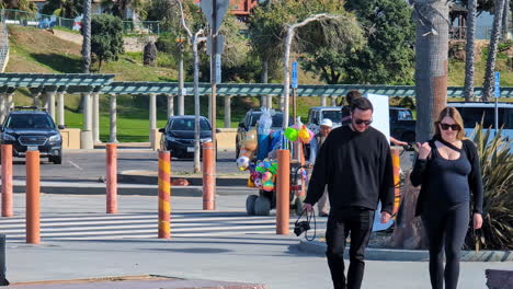 Vendor-Pulling-Cart-With-Beach-Toys-Walking-At-The-Venice-Boardwalk-In-Los-Angeles,-California,-USA