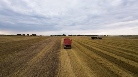 FPV-Aerial-View-of-Tractors-With-Cabin-Wagons-in-Big-Agricultural-Farming-Field-With-Wheat-Crops