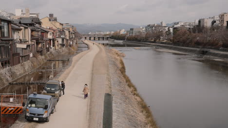 Woman-in-mask-walking-her-dog-along-the-calm-Kamo-River-in-the-usually-crowded-central-Kyoto-on-a-pleasant-winter-day-during-COVID