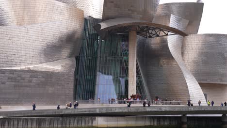 People-Walking-in-Front-of-Guggenheim-Museum-Bilbao,-Spain-by-Nervion-River,-Slow-Motion