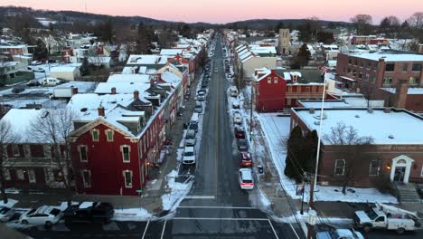 Aerial-straight-flight-over-traffic-on-snowy-main-street-of-small-town-in-America