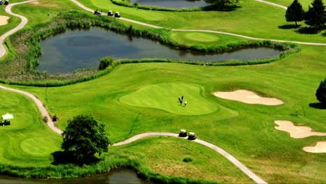 Golf-Players-Walking-On-Green-Grass-Field-Near-Lake-In-Newton,-Surrey,-BC,-Canada