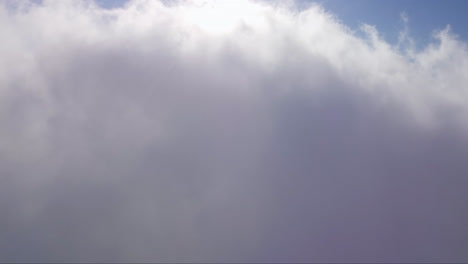 Drone-ascending-view-through-white-clouds-towards-a-bright-sunlight-shining