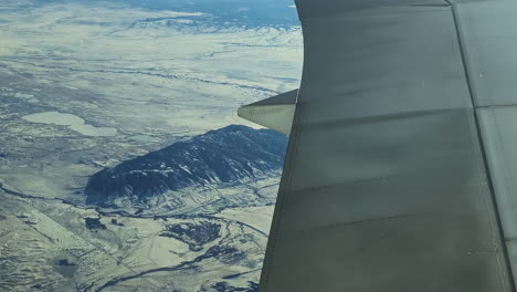 Flying-over-tall-mountains-covered-in-snow-landscape-plane-wing-in-frame
